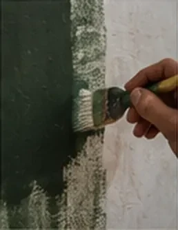 Pinceau appliquant une peinture vert sombre sur un mur clair