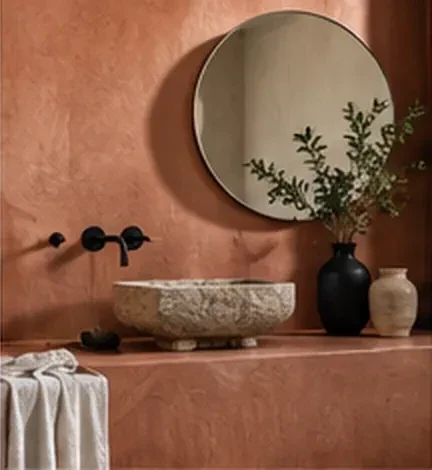 Salle d’eau aux murs en enduit terre cuite, vasque en pierre et miroir rond